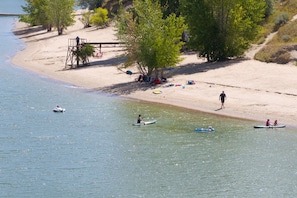 A beach with people paddling in canoes, a lifeguard tower, and a sandy shore with trees. - Mountain Pass Retreat LS54 | Hot Tub| Lakefront (Huntsville)