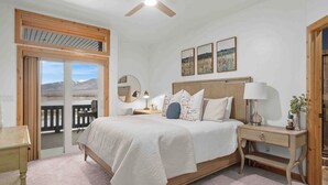 A bedroom with a bed, bedside tables, a ceiling fan, a window with a view, and a door. - Mountain Pass Retreat LS54 | Hot Tub| Lakefront (Huntsville)