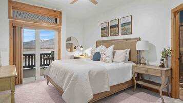 A bedroom with a bed, bedside tables, a ceiling fan, a window with a view, and a door.