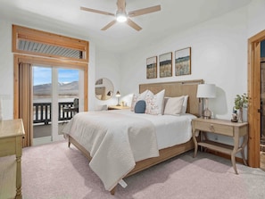 A bedroom with a bed, bedside tables, a ceiling fan, a window with a view, and a door. - Mountain Pass Retreat LS54 | Hot Tub| Lakefront (Huntsville)