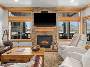 Un salón con chimenea de piedra, muebles de cuero y amplias ventanas con vistas.