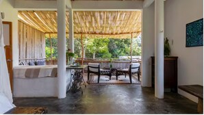 A covered outdoor seating area with a table and chairs, a bench with cushions, and a view of greenery. - Vereda Yelapa: Passion Fruit (Yelapa)