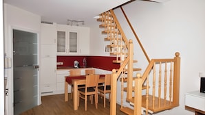 A compact kitchen with a dining area, wooden staircase, and a white cabinet. - 4-Star Vacation Rental in Benediktenwand with Mountain Views and a Balcony (Lenggries)