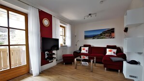 A living room with a red sofa, a coffee table, a TV, and a painting on the wall. - 4-Star Vacation Rental in Benediktenwand with Mountain Views and a Balcony (Lenggries)