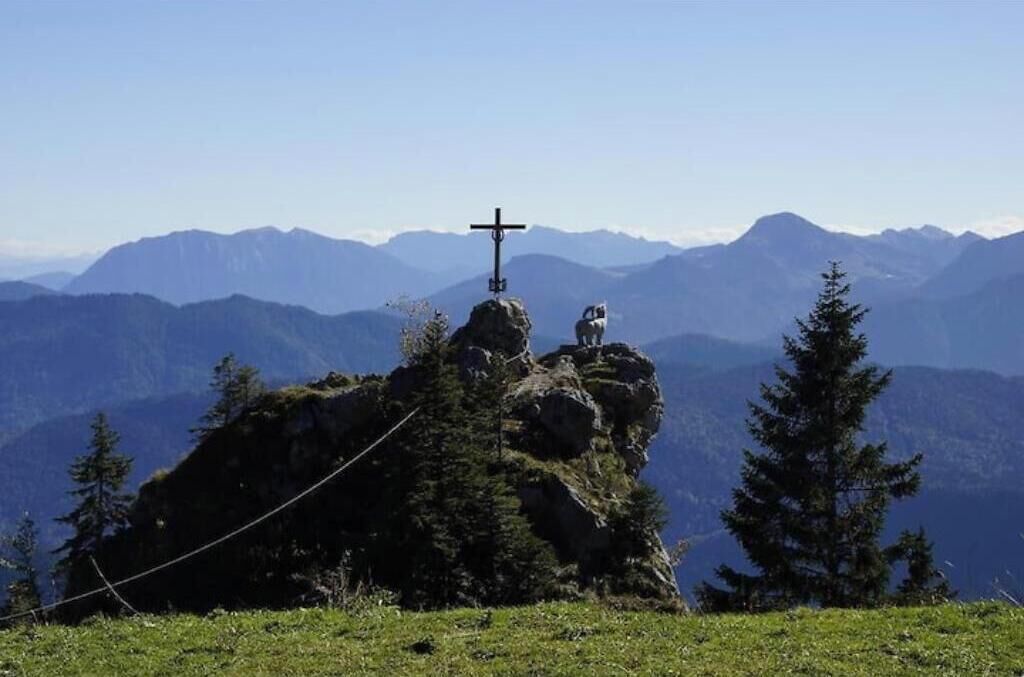 Ein Kreuz auf einem Berggipfel mit freiem Blick auf ferne Berge.