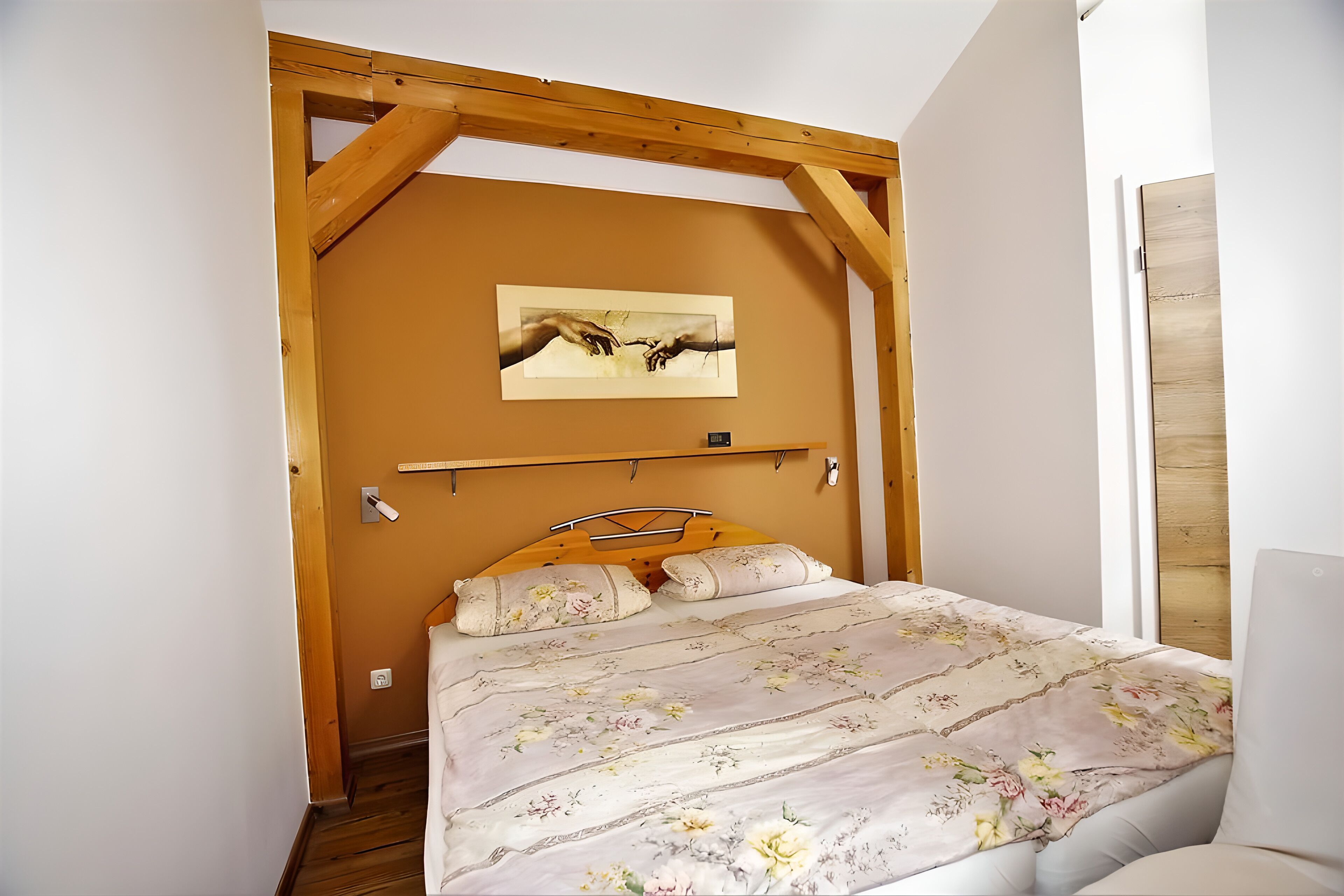 Un dormitorio con techo de madera, una cama con ropa de cama floral, una obra de arte colgada en la pared y una puerta de madera.