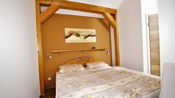 Un dormitorio con techo de madera, una cama con ropa de cama floral, una obra de arte colgada en la pared y una puerta de madera.