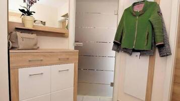 Een hal met een spiegel, een potplant, een beige handtas en een groen jasje aan de muur.