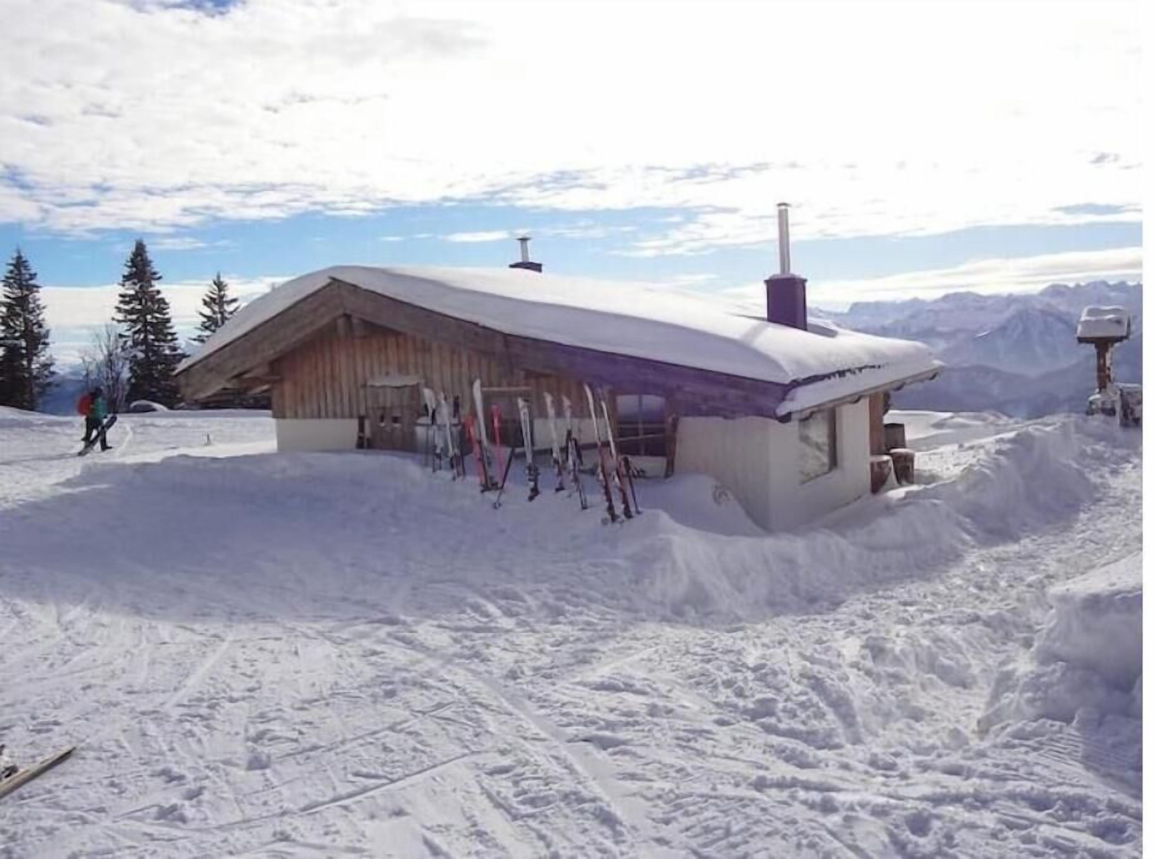 Eine Holzhütte mit geneigtem Dach, umgeben von Schnee, ausgestattet mit Skiausrüstung.