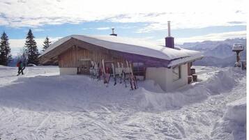 Eine Holzhütte mit geneigtem Dach, umgeben von Schnee, ausgestattet mit Skiausrüstung.