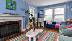 Ein Wohnzimmer mit Kamin, blauer Wand, einer Couch und einem bunten Teppich.
