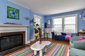 Ein Wohnzimmer mit Kamin, blauer Wand, einer Couch und einem bunten Teppich.
