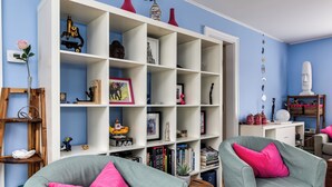 Ein Wohnzimmer mit einem weißen Bücherregal, zwei grünen Sessel mit rosafarbenen Kissen und einer blauen Wand.