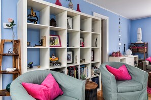 Ein Wohnzimmer mit einem weißen Bücherregal, zwei grünen Sessel mit rosafarbenen Kissen und einer blauen Wand.