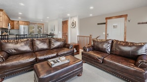 Ein Wohnzimmer mit einem braunen Ledersofa, einem Couchtisch aus Holz und einer Küche im Hintergrund.