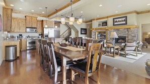 A spacious kitchen with wooden cabinets, a dining area with a large wooden table and chairs, a stone fireplace, and a staircase leading to another level. - Piney Mountain Escape TR5 | Hot Tub | Pool | Games (Eden)