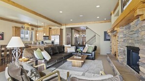 A spacious living room with a fireplace, a kitchen in the background, and a staircase leading to an upper level. - Piney Mountain Escape TR5 | Hot Tub | Pool | Games (Eden)