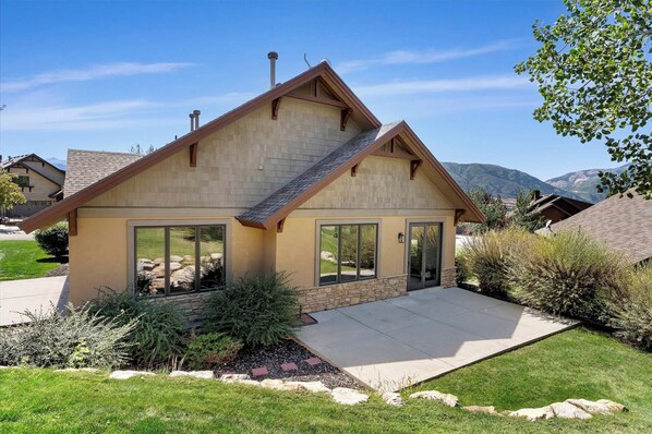 A single-story house with a sloped roof, large windows, and a stone foundation.