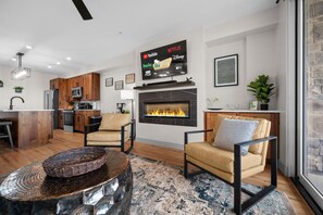 Een moderne woonkamer met een open haard, een keukenhoek en een tv waarop streamingdiensten worden vertoond.