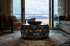 Een woonkamer met uitzicht op het strand, een rieten stoel, een leren fauteuil en een getextureerde salontafel.