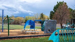 Ein Spielplatz mit Klettergerüsten, einem Picknicktisch und einem umzäunten Bereich.