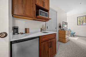 A compact kitchen with wooden cabinets, a microwave, a coffee maker, and a dishwasher. - Water's Edge 102C | Bear Lake| Lakeside Unit (Garden City)