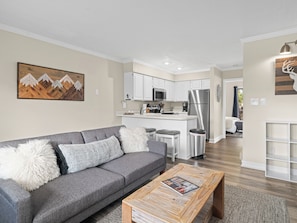 A modern living room with a grey sofa, wooden coffee table, and a kitchen in the background. - Wolf Lodge Hideaway WL206 |Pool, Hot Tub, Golf (Eden)