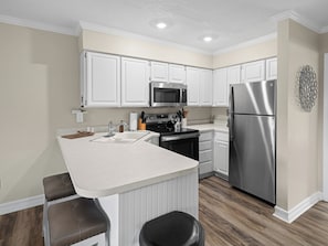 A modern kitchen with white cabinetry, stainless steel appliances, and a central island with bar stools. - Wolf Lodge Hideaway WL206 |Pool, Hot Tub, Golf (Eden)