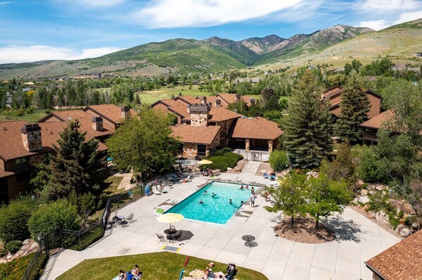 A residential area with a swimming pool surrounded by houses, a patio area, and a view of mountains in the background. - Wolf Lodge Hideaway WL206 |Pool, Hot Tub, Golf (Eden)