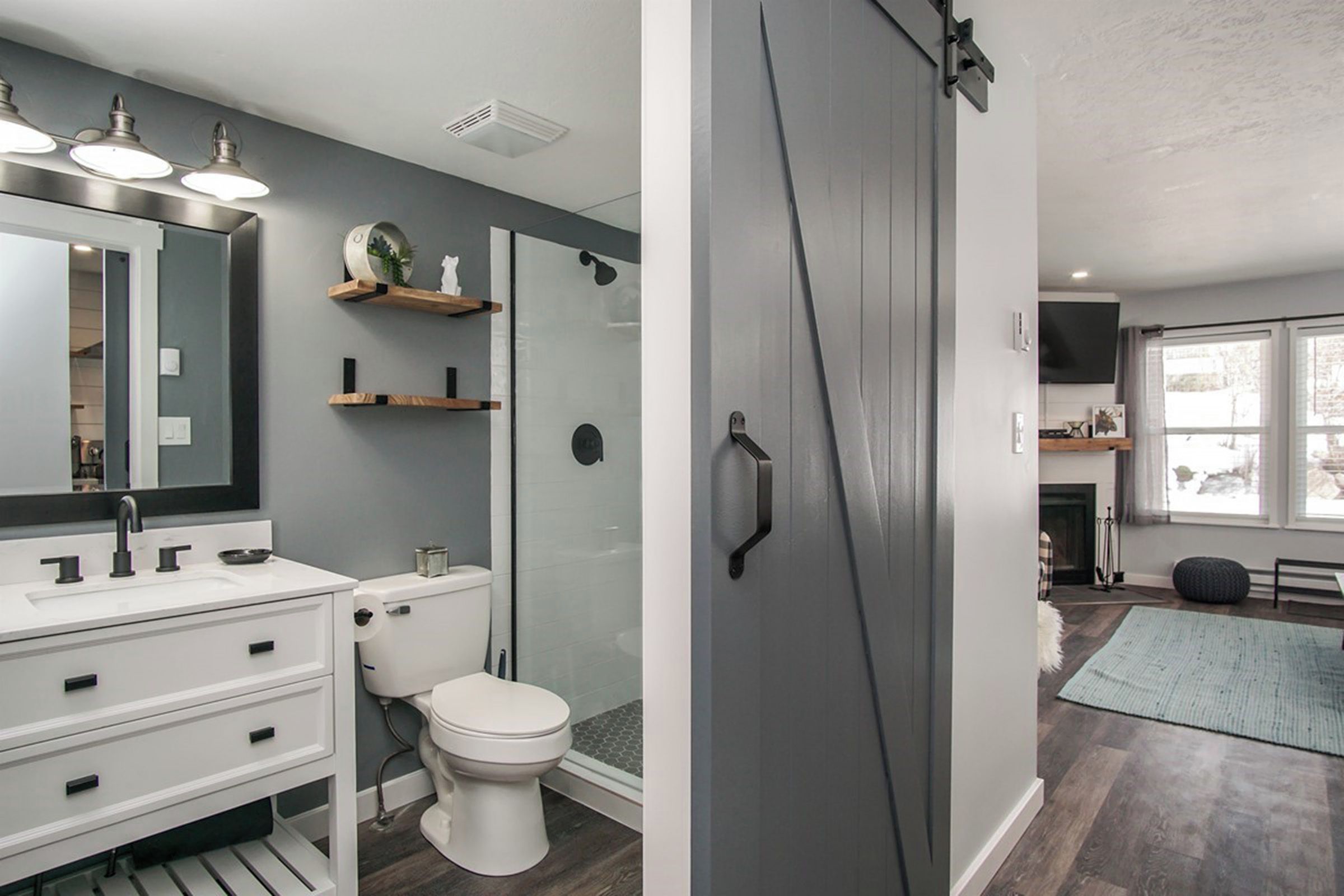 A modern bathroom with a white sink, mirror, and toilet, a glass shower enclosure, and a gray door.