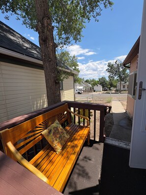 A wooden bench with a cushion, a tree, and a view of a residential street. - Delightful 2 bedroom home in walking distance to downtown, Arkansas River, etc (Cañon City)