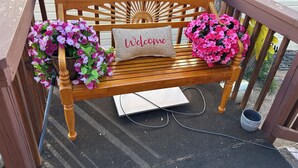 Eine hölzerne Bank mit einem 'Welcome'-Kissen, umgeben von Blumentöpfen.
