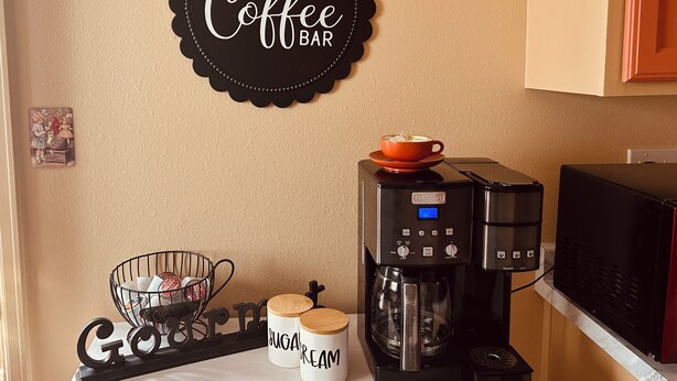 Eine Küche mit Kaffeemaschine, Zucker- und Sahnedosen, einem Schild für die Kaffeebar und einer Wanduhr.