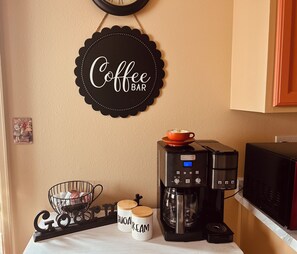 A kitchen with a coffee machine, sugar and cream containers, a coffee bar sign, and a wall clock.