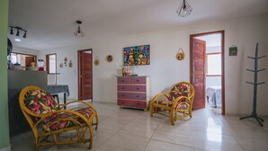 Een ruime woonkamer met rieten meubels, een kleurrijke dressoir en een groot schilderij aan de muur.