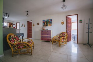 A spacious living room with wicker furniture, a colorful dresser, and a large painting on the wall. - Casa para 8 a 120m da Praia em Porto de Galinhas (Ipojuca)