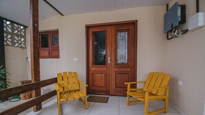 Een houten deur met glaspanelen, twee gele stoelen, een houten bank en een betegelde vloer.
