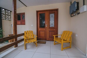 A wooden door with glass panels, two yellow chairs, a wooden bench, and a tiled floor. - Casa para 8 a 120m da Praia em Porto de Galinhas (Ipojuca)