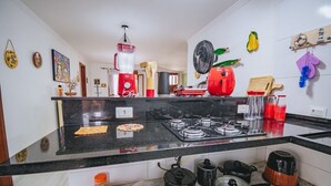 Een keuken met een zwart aanrecht, een gasfornuis, verschillende keukengerei en een rood apparaat.