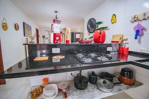 A kitchen with a black countertop, a gas stove, various kitchen utensils, and a red appliance. - Casa para 8 a 120m da Praia em Porto de Galinhas (Ipojuca)