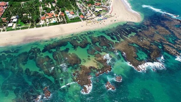 Luchtbeeld van een strand met helder water, rotsformaties en een resort met gebouwen en een zandstrand.