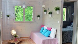 Una habitación acogedora con cama, un banco, una ventana que da a zonas verdes y plantas en macetas en la pared.