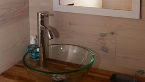 Un baño con lavamanos de cristal, un espejo y una decoración con una flor blanca.