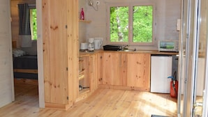 Una cabaña de madera acogedora con kitchenette, cama y ventana con vistas al verdor.