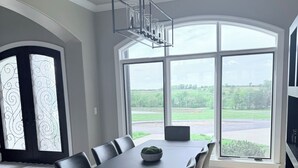A modern dining area with a large table, chairs, and a view of the outdoors through large windows.