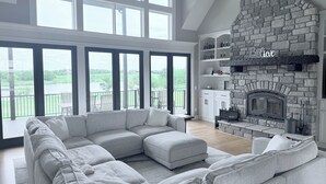 A modern living room with a stone fireplace, large windows, and a view of a lake.