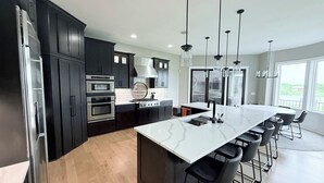 A modern kitchen with dark cabinetry, stainless steel appliances, a large island with bar stools, and pendant lighting.