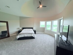 A bedroom with a bed, bedside tables, a ceiling fan, a TV, and windows with a view. - Newly Remodeled, w/ Hot Tub - Lake Views spacious (Wellsville)