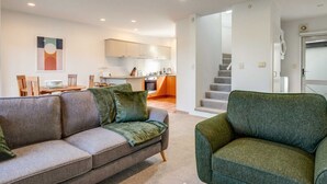 A modern living room with a sofa and armchair, a dining area, and a kitchen in the background. - Henderson Retreat 3BR Townhouse with Parking (Auckland West)