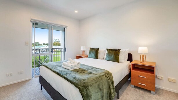 A bedroom with a bed, two bedside tables, a window, and a balcony. - Henderson Retreat 3BR Townhouse with Parking (Auckland West)